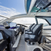 Modern yacht helm on the Galeon 435GTO and seating area with an open panoramic sliding sunroof, featuring three ergonomic captain’s chairs, a sleek dashboard with integrated displays, and waterfront city skyline in the background.