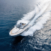 Aerial view of a Jeanneau Leader 46 yacht cruising at speed with its sliding sunroof open, featuring a spacious foredeck sunpad and leaving a wide wake across deep blue water.
