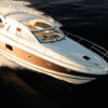 Aerial view of a Prestige 440S yacht cruising at speed with its sliding sunroof fully open, revealing the light-filled helm area, and featuring a sleek bronze-and-white hull gliding over dark water.