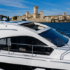 White Sessa C42 yacht cruising near a historic waterfront castle, featuring an open panoramic sliding sunroof and sleek side windows under a clear blue sky.