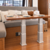 Electric table lift kit NL2388-PAIRE-B installed in a yacht saloon on a wooden floor - two synchronized 3-stage rectangular aluminium legs supporting a varnished wood dining table in front of a U-shaped bench